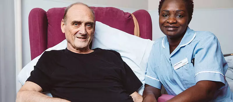 man at home with a nurse sitting by his side