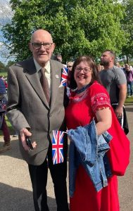 Joe in a suit and Dawn in a red dress smiling at the camera holding a Union Jack flag
