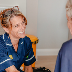 Nurse in a navy uniform smiling at a patient opposite her