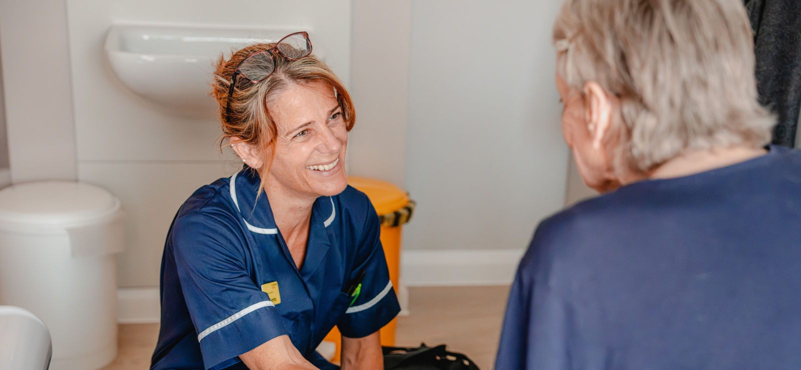 Nurse in a navy uniform smiling at a patient opposite her